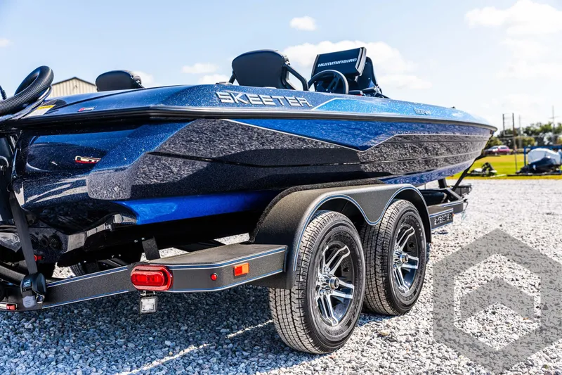 Slide: The Image of 2025 Skeeter ZXR 21 boat on trailer, blue and black design, parked on gravel. - 13