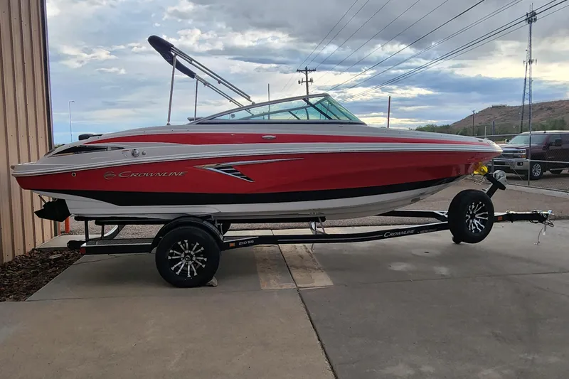 Slide: The Image of 2024 Crownline 210SS boat in red on a trailer, parked outdoors. - 4