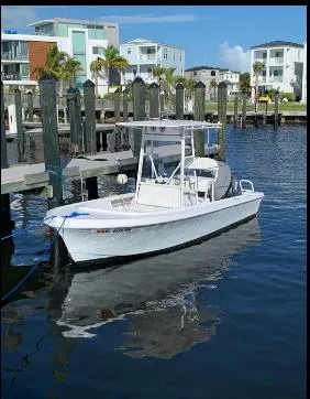 Slide: The Image of 1993 Mako 19 boat docked in a marina with modern buildings in the background. - 2