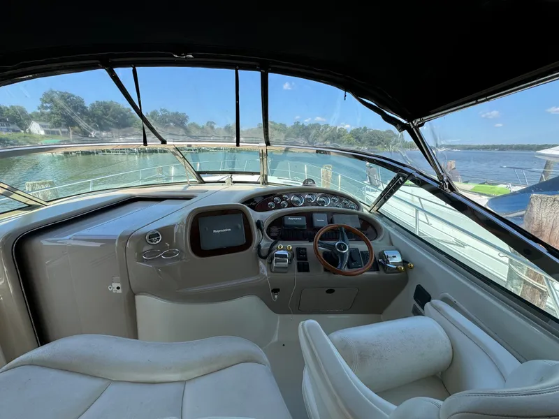 Slide: The Image of 1999 Sea Ray 380 Sundancer cockpit with steering wheel and navigation controls, docked by a scenic lake. - 13