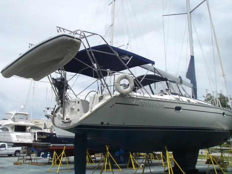 Slide: The Image of 2001 Jeanneau 45.2 sailboat on stands, with blue canopy and dinghy, in a marina. - 23