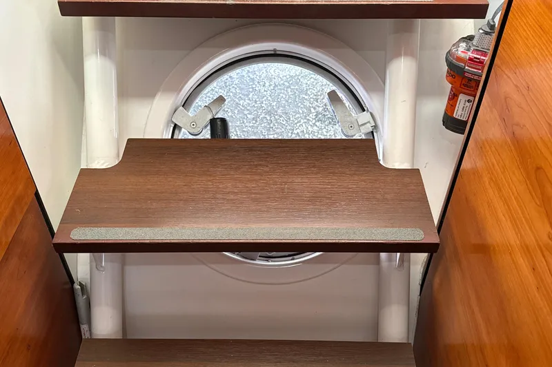 Slide: The Image of Wooden steps inside a 2010 Outremer 49 yacht, featuring a round porthole and safety equipment. - 23