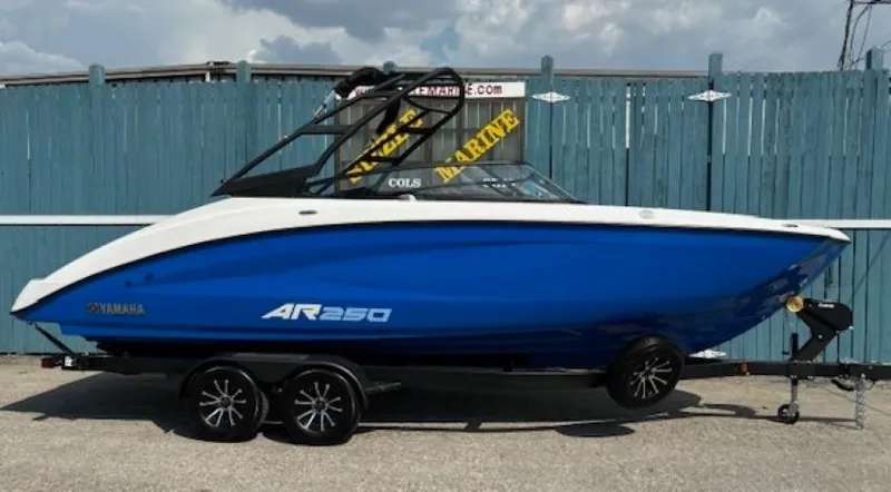 The Image of 2025 Yamaha Boats AR250, blue and white, on trailer, parked by a blue fence. - 0