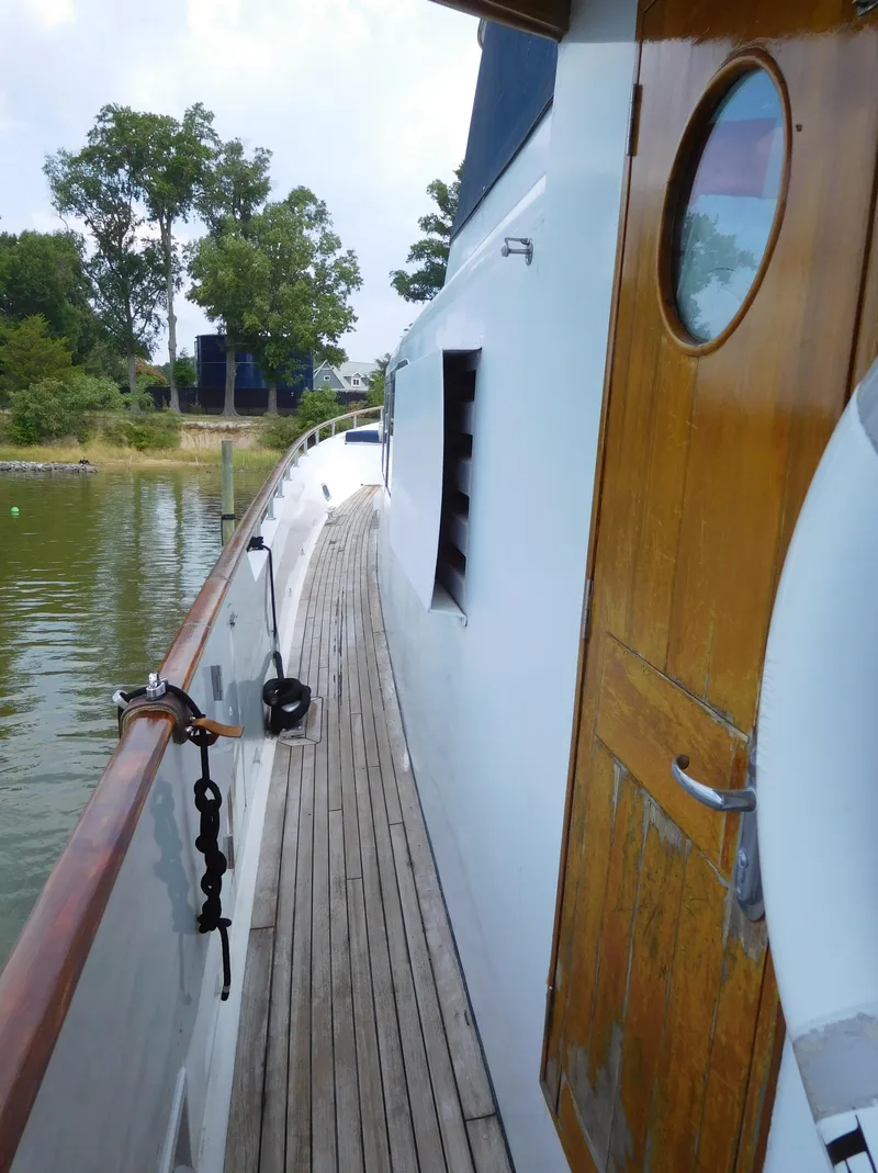 Slide: The Image of 1983 Cheoy Lee 90 cockpit motor yacht, wooden deck and cabin door, docked by lush greenery. - 4