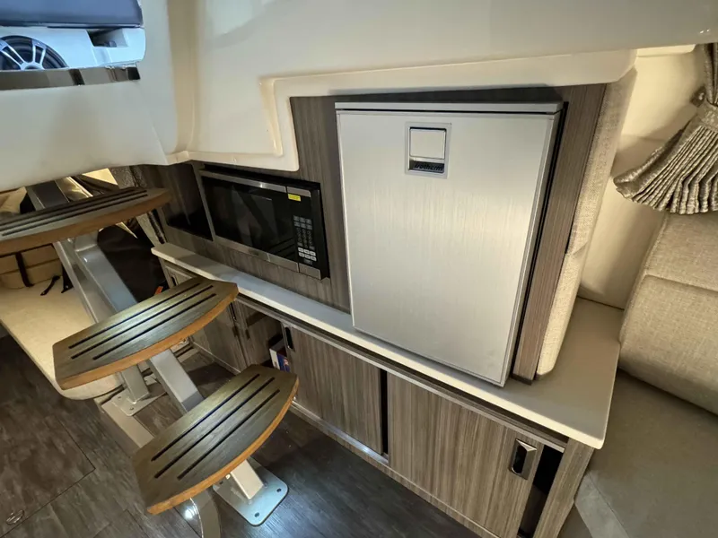Slide: The Image of 2024 Sea Ray 320DA interior with microwave, fridge, and wooden steps. - 10
