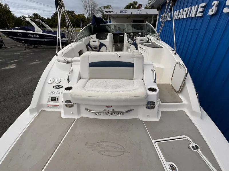 Slide: The Image of 2012 Chaparral 244 Sunesta boat interior with seating and helm, docked near a blue building. - 4
