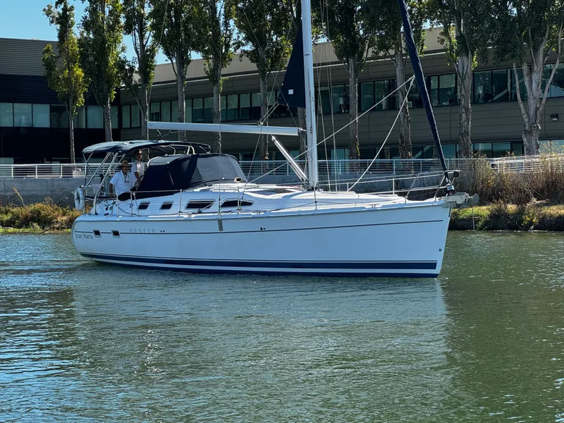 Slide: The Image of 2007 Hunter 41 sailboat cruising on a calm waterway near modern buildings. - 0