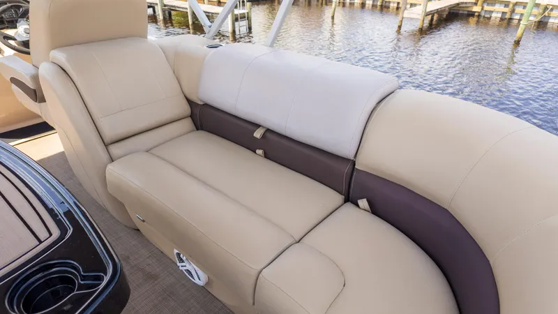 Slide: The Image of 2019 Sun Tracker 24 DLX Party Barge interior seating, beige and brown upholstery, near water. - 8