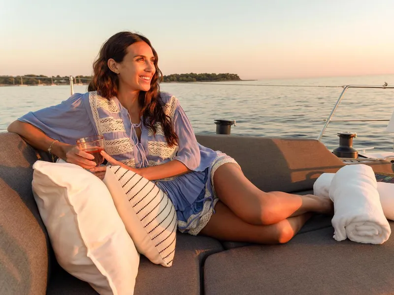 Slide: The Image of Woman relaxing on a 2025 Hanse 410 yacht at sunset, holding a drink. - 5