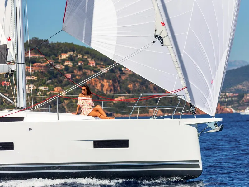 Slide: The Image of 2025 Hanse 410 yacht sailing with woman relaxing on deck, coastal background. - 44