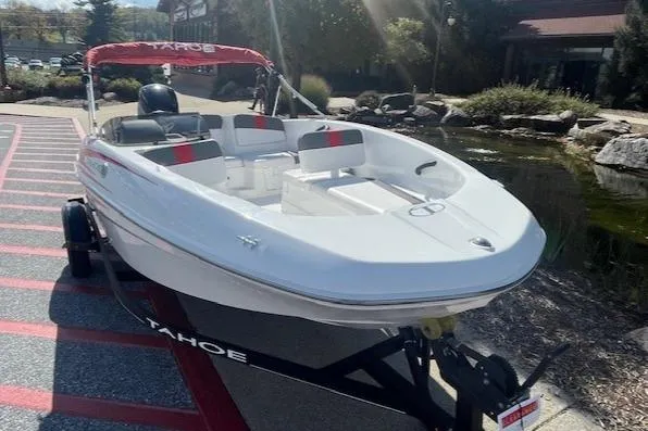Slide: The Image of 2024 Tahoe T16 boat on trailer, white with red accents, parked outdoors. - 2