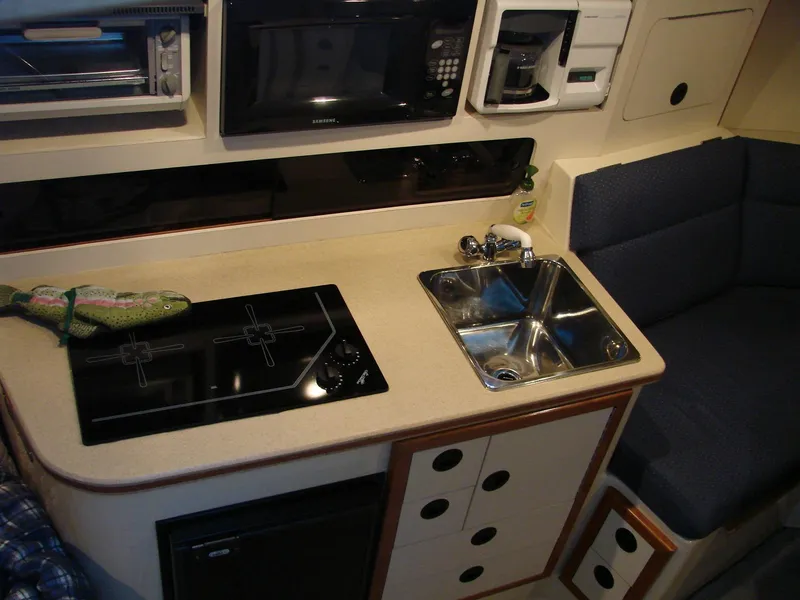 Slide: The Image of 2005 Albin Tournament Express boat kitchen with stove, sink, and seating area. - 34