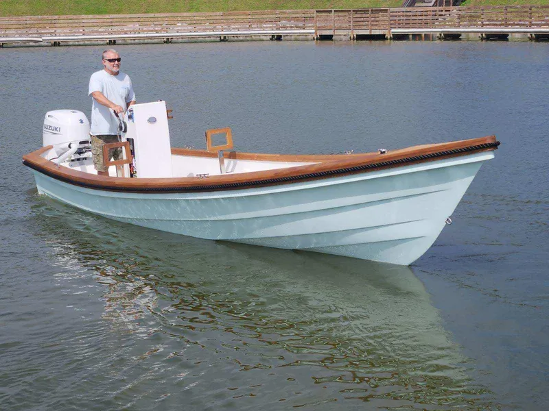 Slide: The Image of 2024 Caribiana Maracas boat on water, man steering, wooden trim, serene setting. - 4