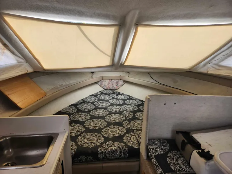 Slide: The Image of 1999 Bayliner 2452 Ciera Express cabin interior with patterned bedding and compact kitchenette. - 8