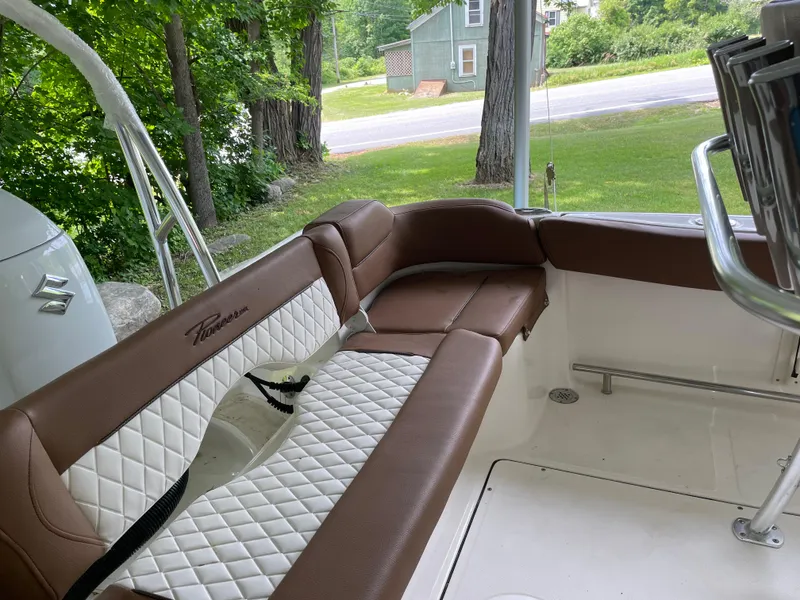 Slide: The Image of 2024 Pioneer 222 Islander boat interior with brown and white seating, near a green landscape. - 25