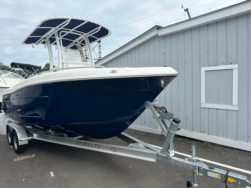 The Image of 2025 Robalo R222 Center Console boat on trailer, parked near a gray building. - 0