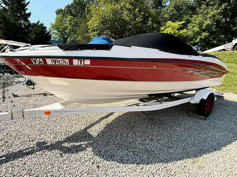 Slide: The Image of 2010 Bayliner 215 BR boat on trailer, red and white, parked on gravel. - 2