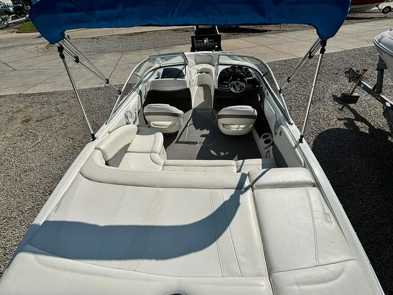 Slide: The Image of 2010 Bayliner 215 BR boat with white interior and blue canopy, parked on gravel. - 23