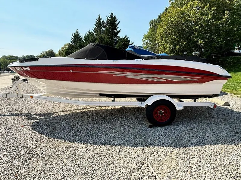 Slide: The Image of 2010 Bayliner 215 BR boat on trailer, red and white, parked on gravel. - 4
