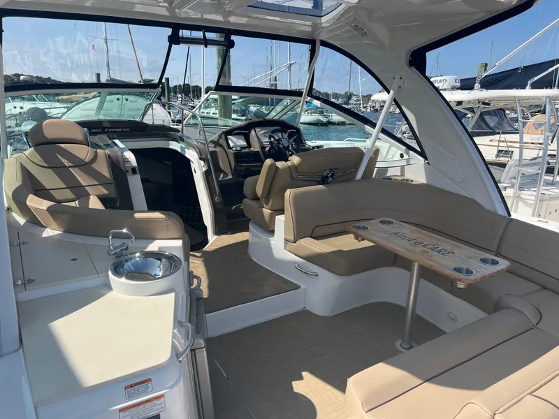 Slide: The Image of 2015 Cruisers Yachts 350 Express interior with beige seating and helm, docked at marina. - 10