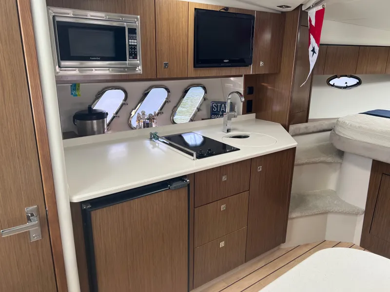 Slide: The Image of 2015 Cruisers Yachts 350 Express interior with kitchenette, microwave, and TV. - 15