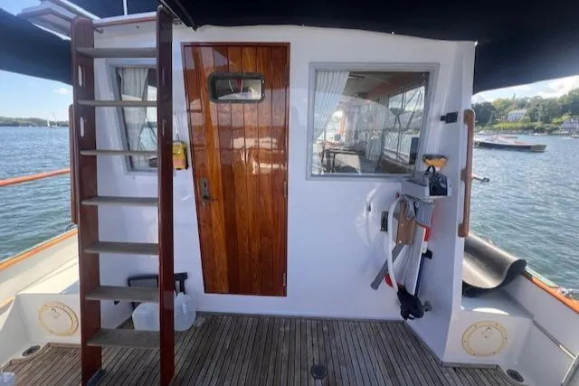 Slide: The Image of 1980 Grand Banks 32 Flybridge Trawler deck with wooden door and ladder, overlooking water. - 15