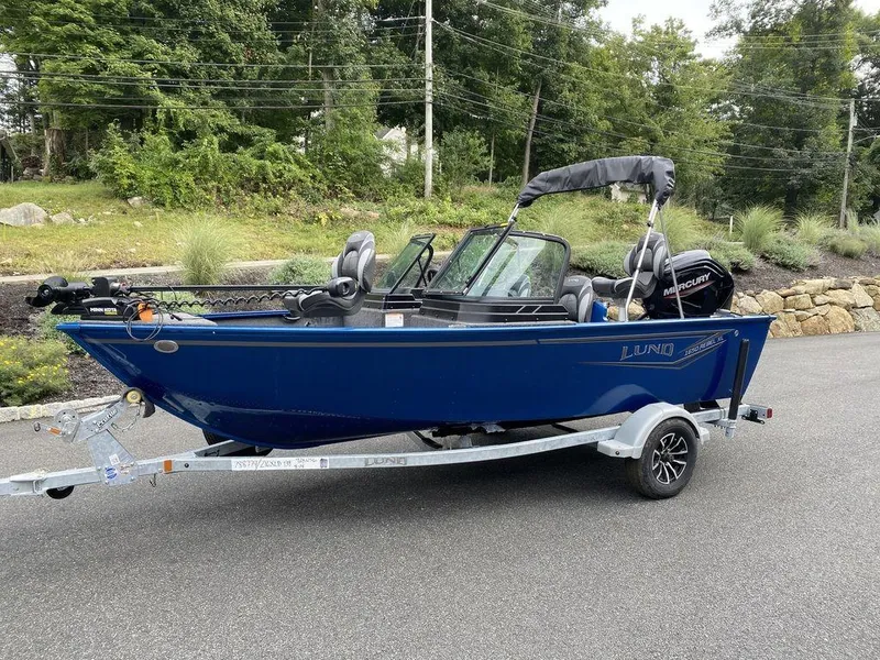 Slide: The Image of 2025 Lund 1650 Rebel XL boat on trailer, parked on road, surrounded by greenery. - 8