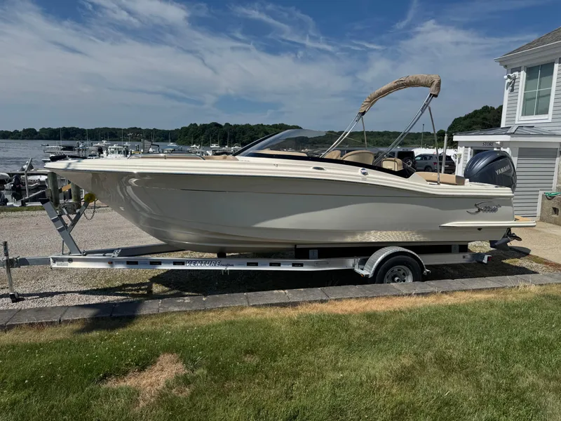 Slide: The Image of 2025 Scout 215 Dorado boat on trailer, parked near waterfront, under clear blue sky. - 16