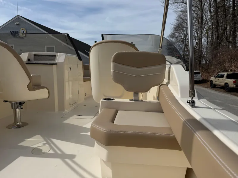 Slide: The Image of 2025 Scout 215 Dorado boat interior with beige seating and helm, parked outdoors. - 22
