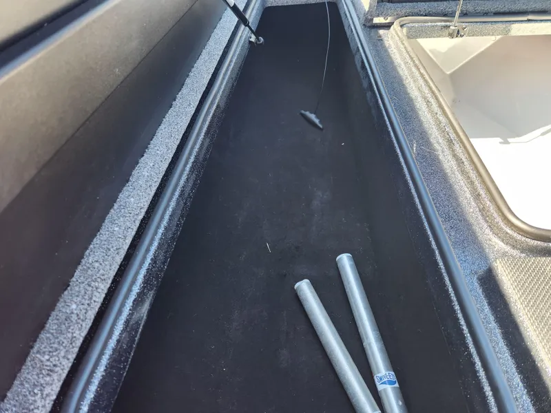 Slide: The Image of 2024 Triton 18 TrX boat storage compartment with rods and black interior. - 11
