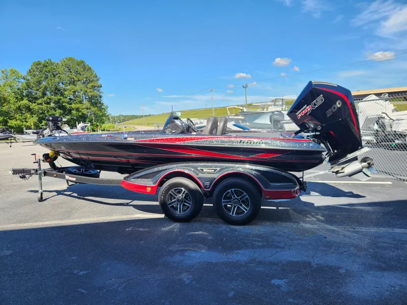 Slide: The Image of 2024 Triton 18 TrX bass boat with trailer, parked outdoors under clear blue sky. - 2