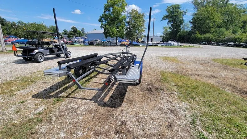 Slide: The Image of Trailer for 2017 MasterCraft X23 boat on gravel lot with trees and golf cart nearby. - 14