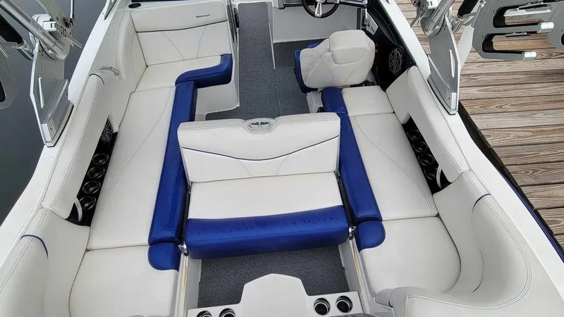 Slide: The Image of 2017 MasterCraft X23 boat interior with white and blue seating, docked by wooden pier. - 15