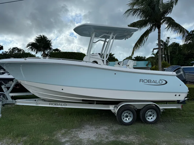 The Image of 2025 Robalo R230 Center Console boat on trailer, parked near palm trees. - 1