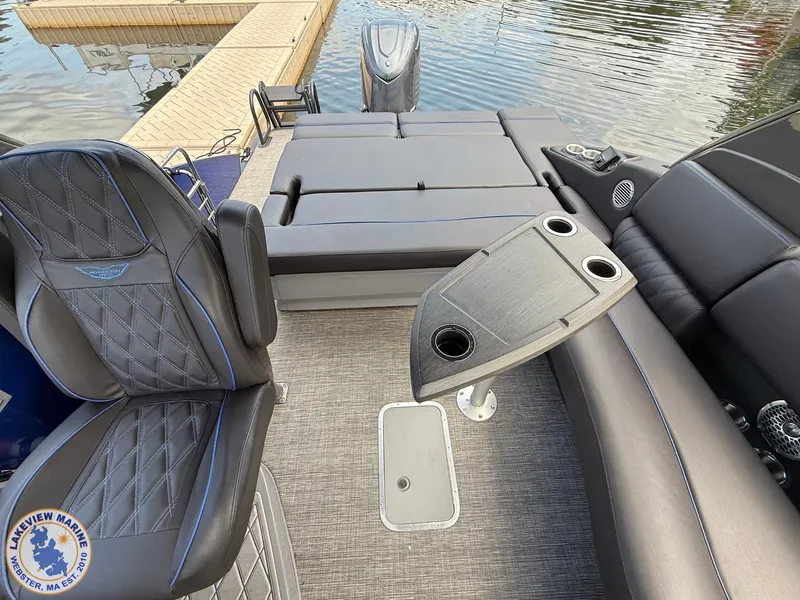 Slide: The Image of 2024 Bennington RX 23 RXSBA boat interior with luxury seating and table, docked by the water. - 6