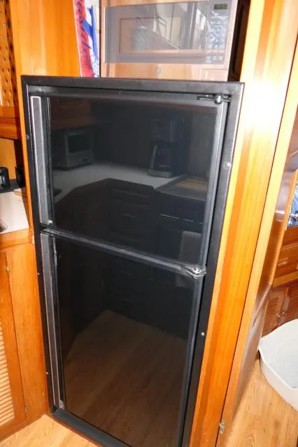 Slide: The Image of 1986 Nova 36 Sundeck interior with a black refrigerator and wooden cabinetry. - 22