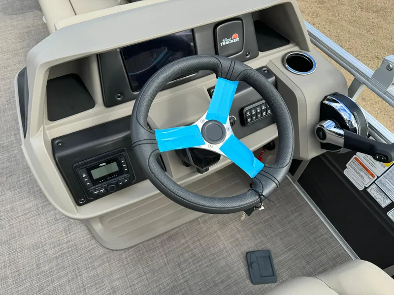 Slide: The Image of 2024 Sun Tracker Fishin' Barge 20 DLX steering console with modern controls and blue-accented wheel. - 16
