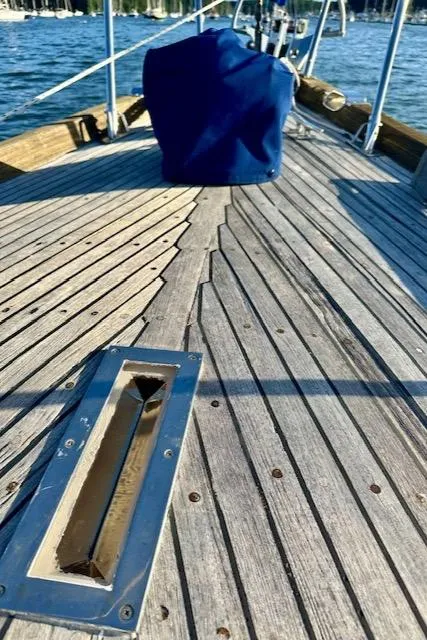Slide: The Image of 1986 Mason 33 sailboat deck with blue cover, wooden planks, and water view. - 13