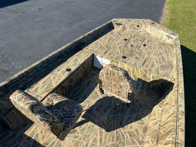 Slide: The Image of 2025 Lowe Roughneck 1760 boat with camouflage seating and deck, parked on pavement. - 11