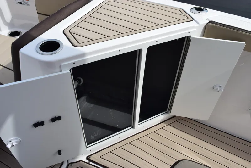 Slide: The Image of 2025 Yamaha Boats 222 FSH Sport E storage compartment with open doors and cup holders. - 15