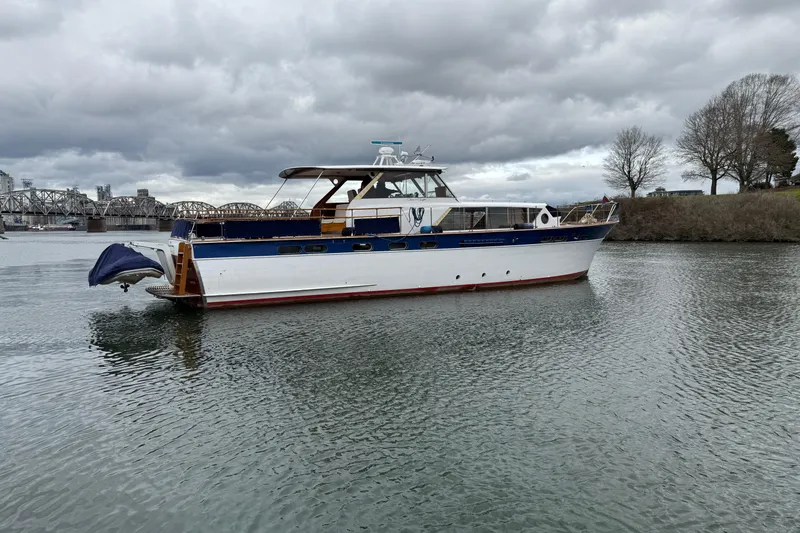 Slide: The Image of 1961 Chris-Craft 55 yacht on a calm river with overcast skies and a bridge in the background. - 18