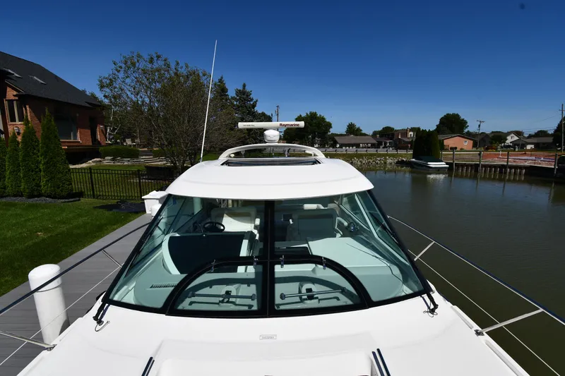 Slide: The Image of 2010 Sea Ray 450 Sundancer yacht docked by a serene waterfront, under a clear blue sky. - 9