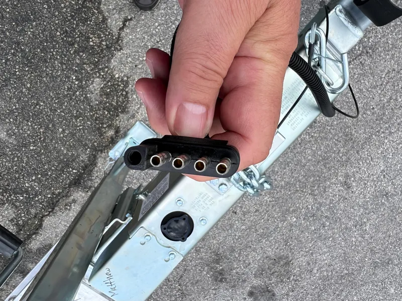 Slide: The Image of Hand holding a 2024 trailer connector plug above a metal hitch on asphalt. - 8
