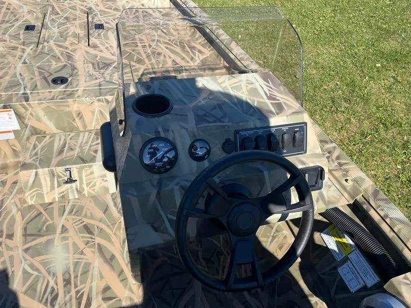 Slide: The Image of 2025 Lowe Roughneck 1760SC boat dashboard with camouflage design and steering wheel. - 6