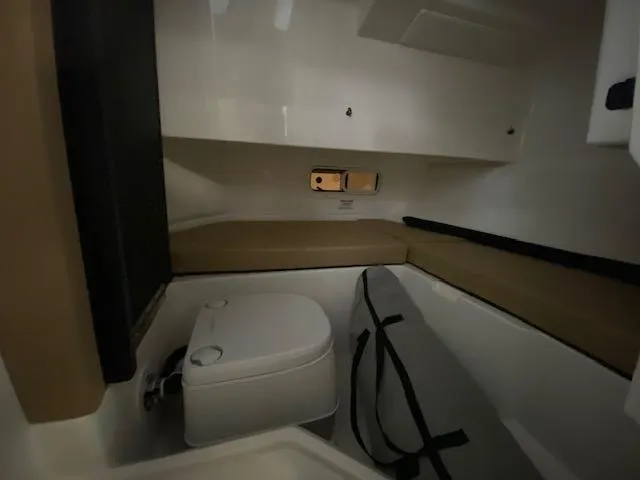 Slide: The Image of 2024 Sea Ray SDX 250 Outboard interior cabin with compact toilet and seating area. - 15