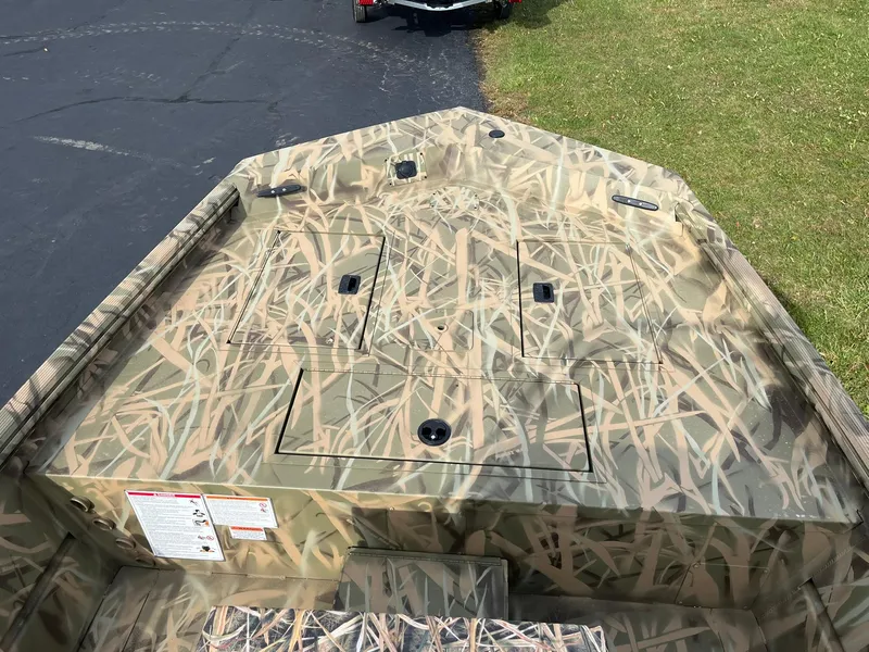 Slide: The Image of 2025 Lowe Roughneck 1860 Tunnel Jet boat with camouflage design on grass and pavement. - 9
