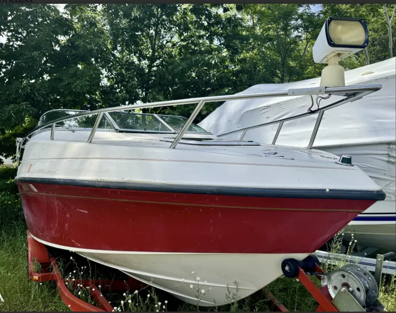 The Image of 1992 Crownline 210 CCR boat with red hull on trailer, parked outdoors. - 0