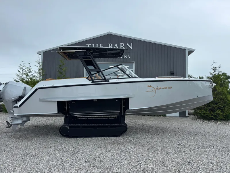 Slide: The Image of 2025 Iguana Bow Rider boat with tracks, parked on gravel near a building. - 2