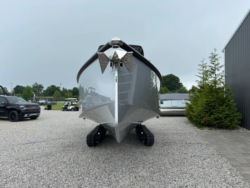 Slide: The Image of 2025 Iguana Bow Rider boat with tracks, parked on gravel near trees and vehicles. - 8