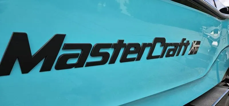 Slide: The Image of 2025 MasterCraft XT24 boat logo on a vibrant blue hull. - 2